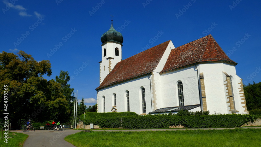 sehr schöne Dorfkirche in Poltringen auf grüner Wiese mit Bäumen unter blauem Himmel und Radfahrern