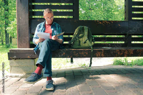 Obraz na plátně A man in glasses is reading a letter while sitting on a park bench
