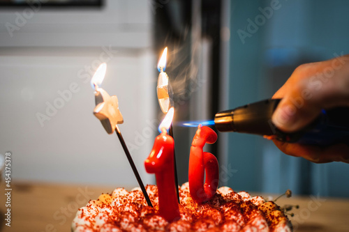 Human hand using a blowtorch to light a candle in a birthday cake photo