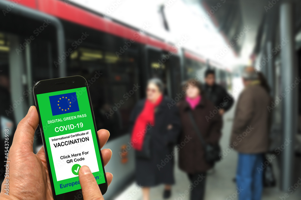 A man at a tram stop holds a smartphone with the European Union digital green pass for Covid-19 in his hand. Safe travel concept during the Coronavirus and the Green pass