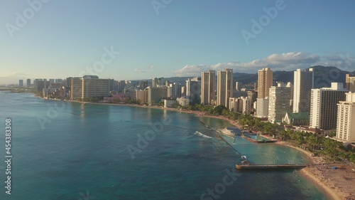 Panning aerial drone slowly flying over a colorful Honolulu Skyline while Sunset in Oahu, Hawaii with Waikiki Beach Shooting from a bird's eye view. Magnificent mountains of Hawaiian island of Oahu.