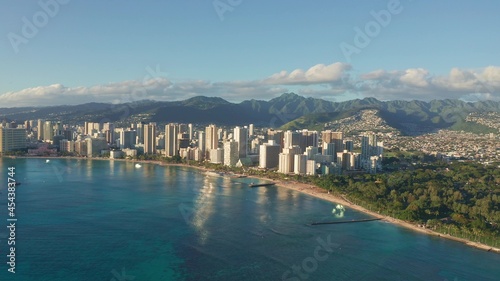 Panning aerial drone slowly flying over a colorful Honolulu Skyline while Sunset in Oahu, Hawaii with Waikiki Beach Shooting from a bird's eye view. Magnificent mountains of Hawaiian island of Oahu.