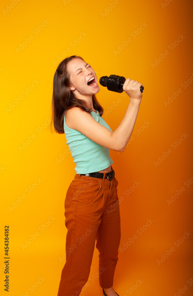 girl brunette teenager, 15 years holding a microphone in his hands depicting singing with his mouth open. The concept of postcards or a vocal lesson at school, back to school girl brunette teenager, 15 years holding a microphone in his hands depicting singing with his mouth open. The concept of postcards or a vocal lesson at school, back to school