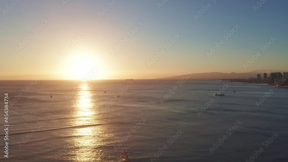 Aerial flight over the ocean at sunset. The drone flies into the distance against the backdrop of a sunny path. View of yachts and boats. A warm sunny day on the tropical island of Oahu Hawaii.