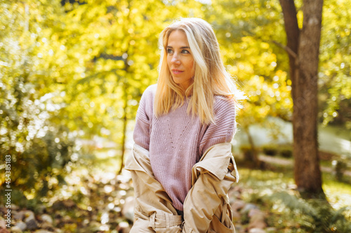 Caucasian blonde woman smiling happily on sunny autumn or spring day outside walking in park.