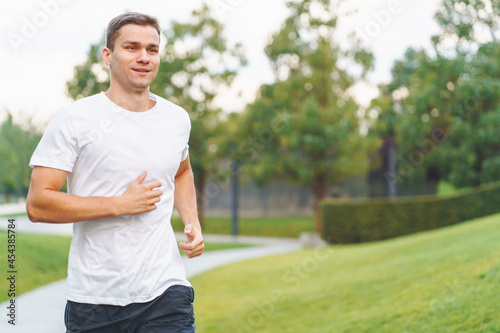 Young sports athlete man in white t-shirt run in the morning in modern park.