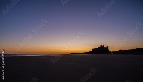 Fototapeta Naklejka Na Ścianę i Meble -  The iconic Bamburgh Castle in Northumberland at sunrise, with the nearby beach deserted.
