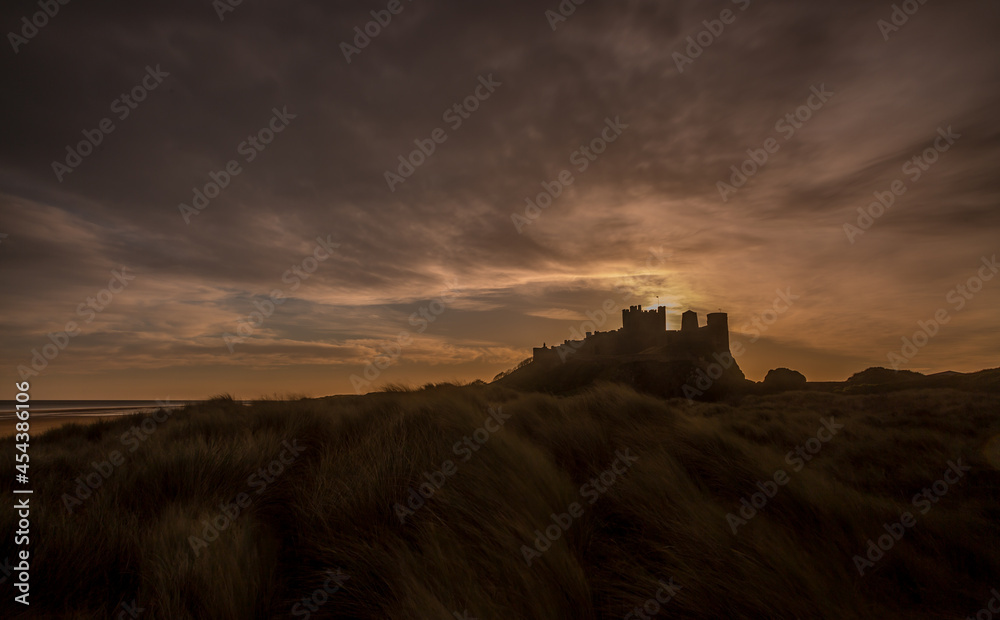The iconic Bamburgh Castle in Northumberland at sunrise, with the nearby beach deserted.
