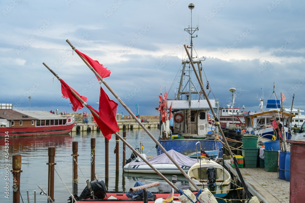 Red flags and fishing boats at the dock in the port of Sassnitz on the island of Rugen in the Baltic Sea against a cloudy sky, travel and tourist destination, copy space, selected focus