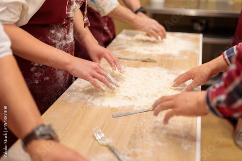 The hands of several people are kneading the dough on the table. Mix a raw egg with flour. Close-up.