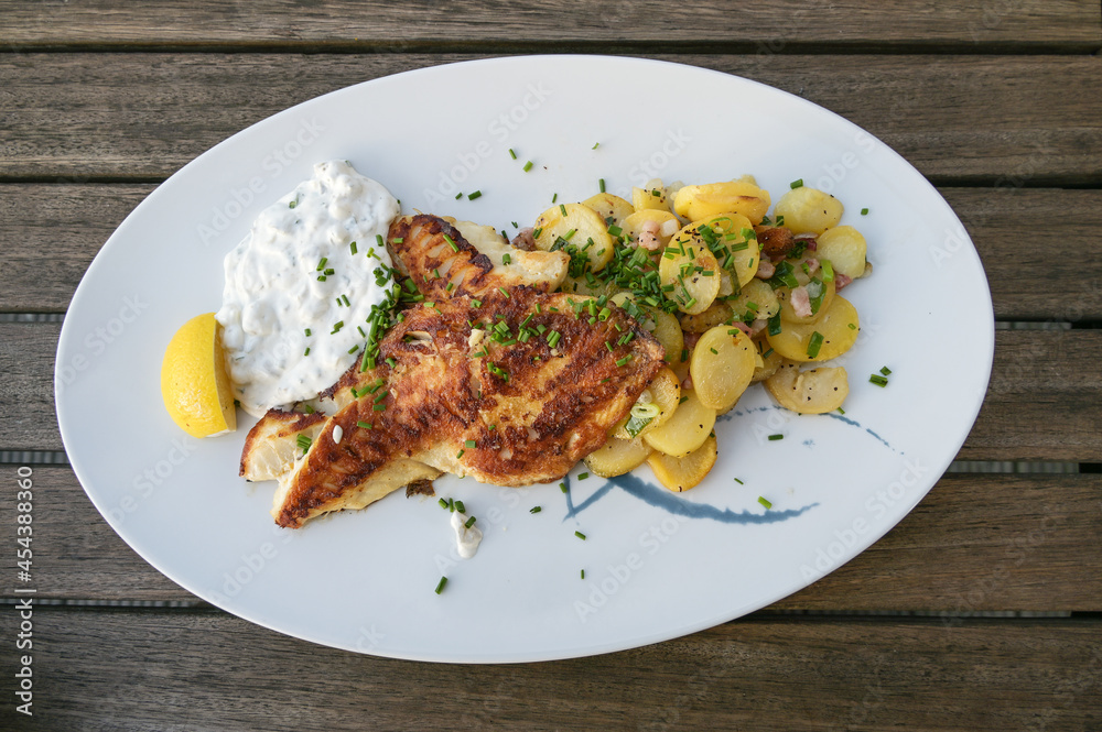 Juicy roasted redfish fillet with fried potatoes and remoulade dip on a plate and on a rustic wooden table, view from above