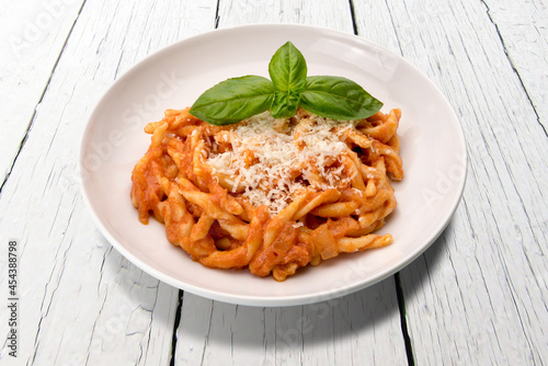 Strozzapreti macaroni pasta with tomato sauce, basil leaves and grated parmesan in white plate on white wooden table photo