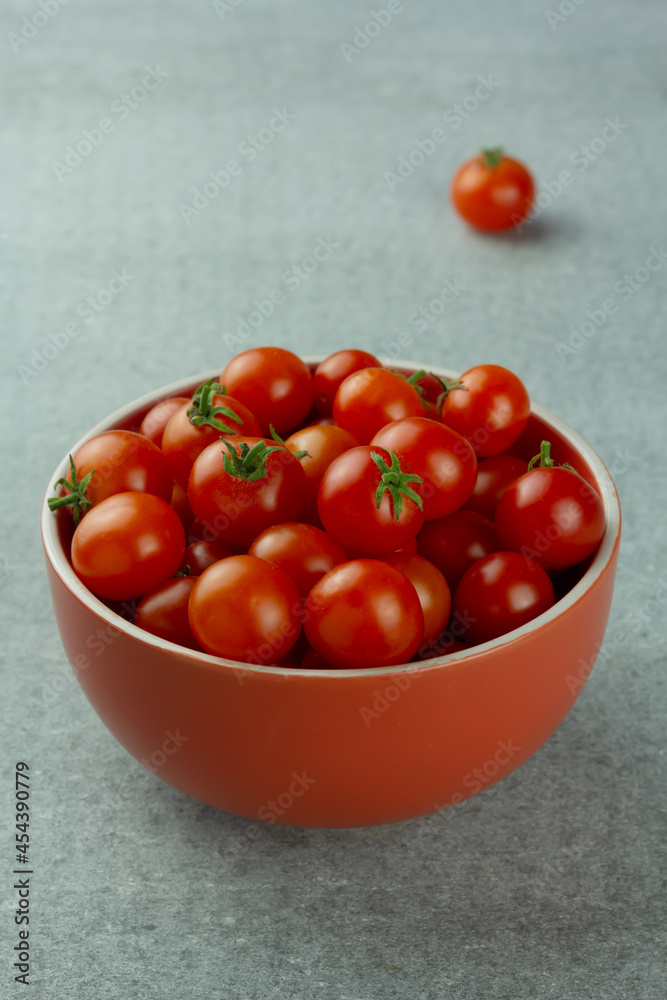 Cherry tomatoes in a red bowl on grey background. Selective focus Cherry tomatoes in a red bowl on grey background. Selective focus