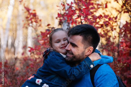 close up happy family portrait. happy smiling father with dark hair hold his little daughter in blue jacket at autumn forest background. 