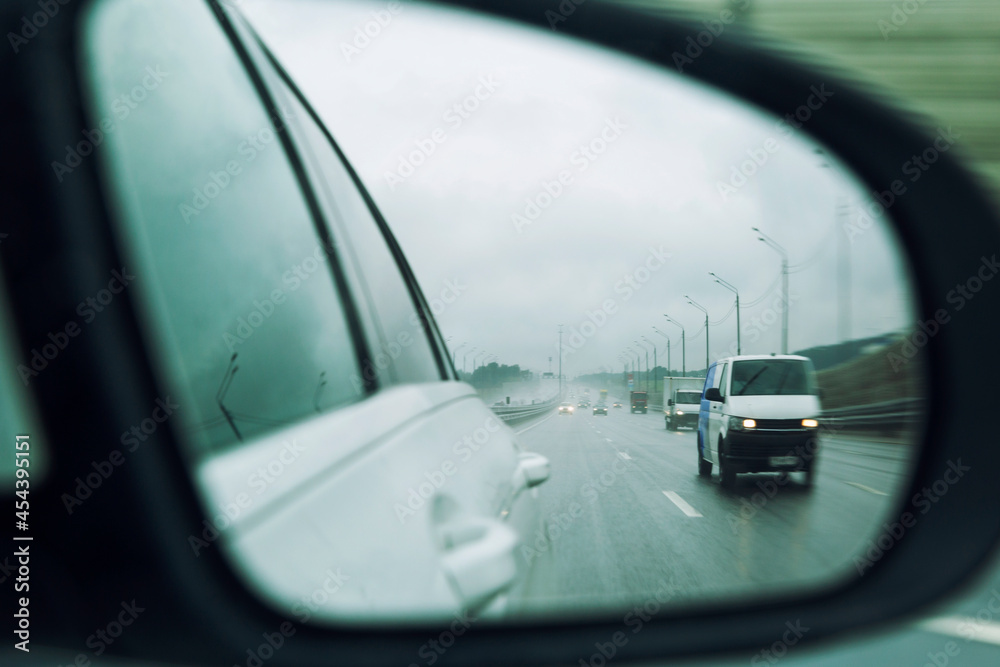 Cars on the highway in the rain in the side mirror. Close-up.