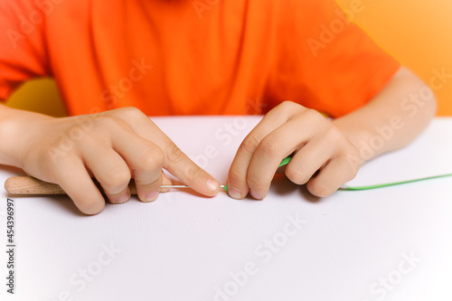 the hands of a boy in close up who inserts thin paper strips into a twisting tool in the quilling technique