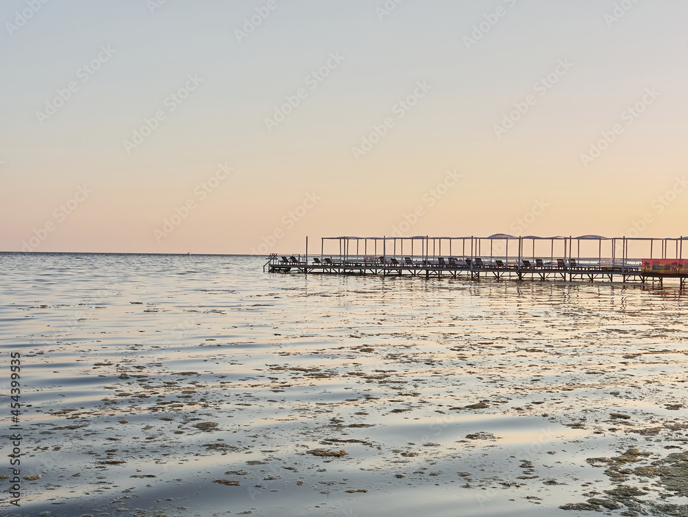 Obraz premium Evening sea. Empty pier, lots of algae and crimson sun.