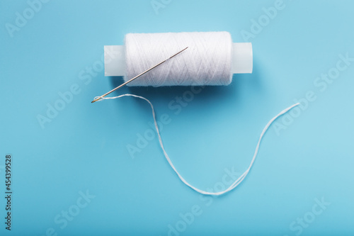 A skein of white thread with a needle on a blue background