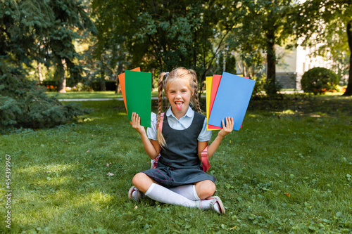 Education concept. Cute smiling schoolgirl sitting on the grass. Happy little girl holding books photo