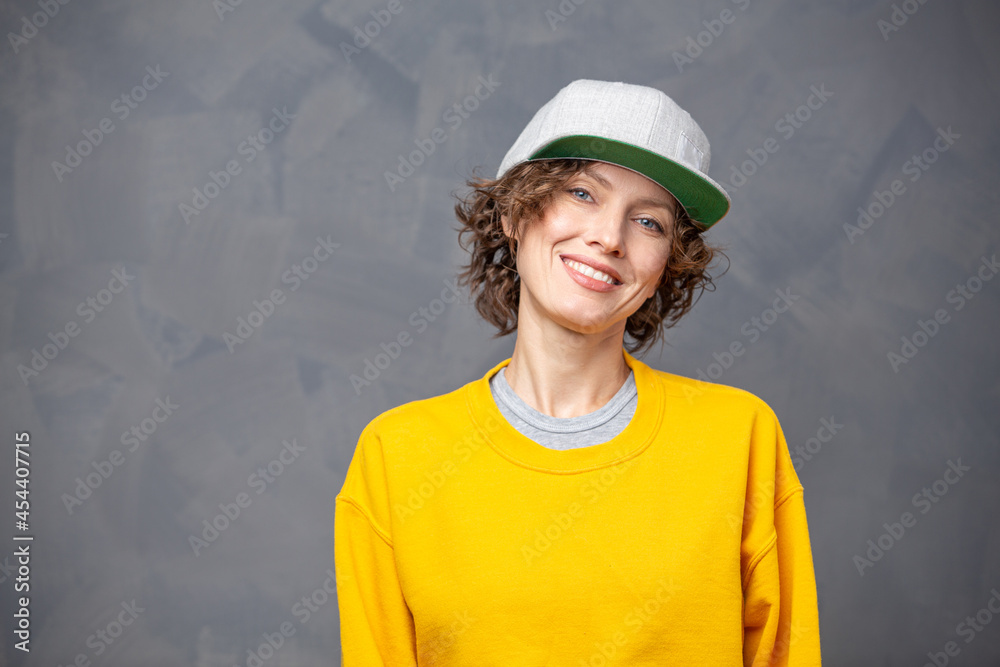 Autumn mood! Portrait of happy smiling woman  with short brunette curly hair wearing yellow sweater and a hat over grey wall background