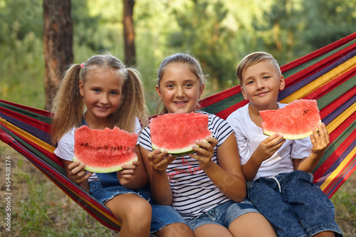 children eat watermelon and joke  in the fresh air  sitting on a hammock