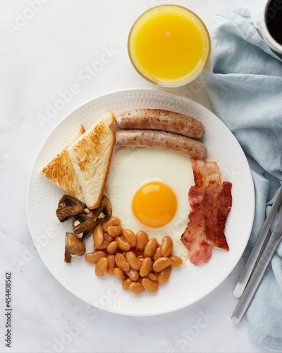 Horizontal flat lay of traditional rustic nutritious irish cuisine food. Fried eggs, grilled sausages, roasted mushrooms, toast, kidney beans, hot coffee and fresh orange juice. Light background