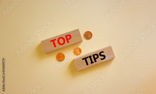 Top tips symbol. Concept words 'top tips' on wooden blocks on a beautiful white background, metallic coins. Business and top tips concept, copy space.