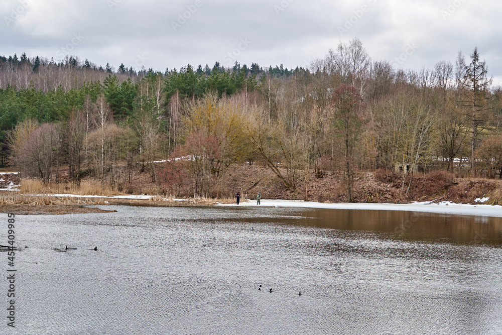Lake in early spring. Some people are fishing on the remains of the ice. 