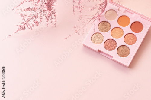 Palette of shadows and plants frame. Pink background. Space for text. Concept of makeup and makeup artist