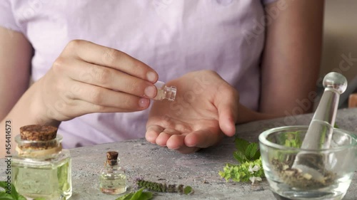 Teenage girl's hands taking homeopathic pills or globules from a glass bottle, with essential oils and herbs in the foreground photo