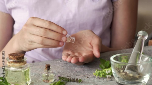 Teenage girl's hands taking homeopathic pills or globules from a glass bottle, with essential oils and herbs in the foreground