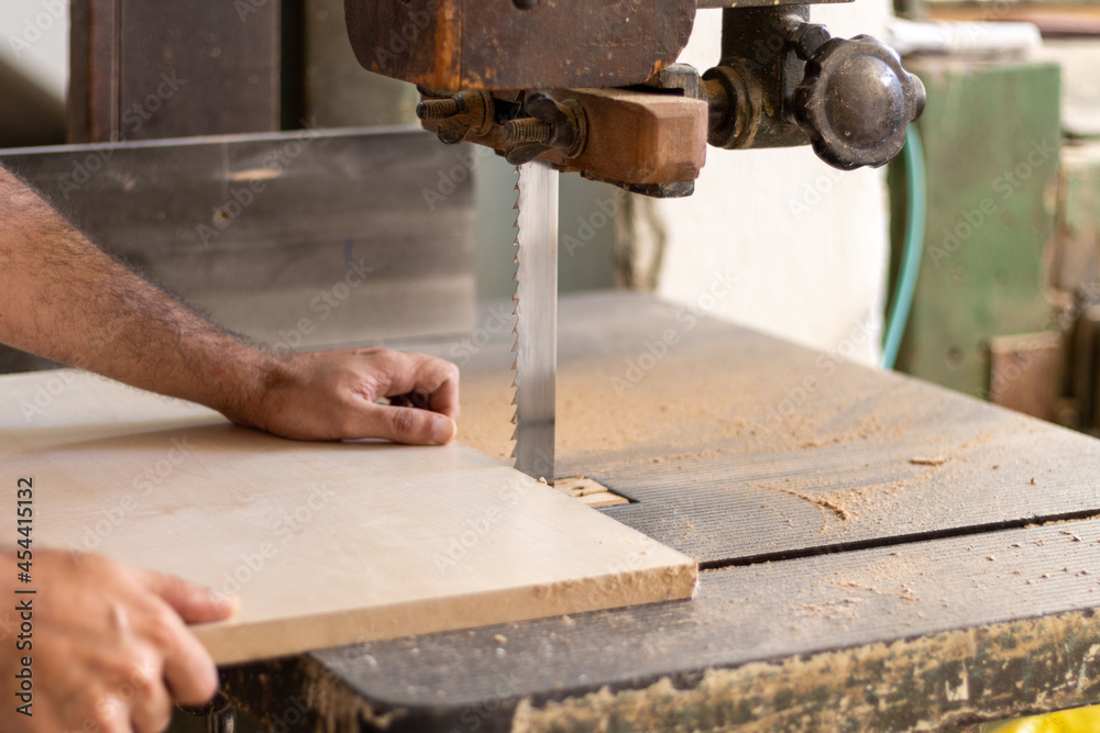 Carpenter woodworker is cutting wood with industrial electric wood cutting machine for furniture making in workshop