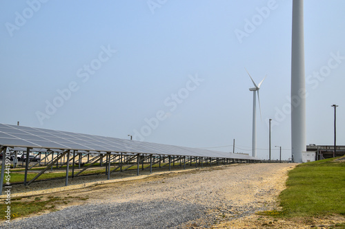 View of a long array of solar panels with an electric generating wind turbine in the background