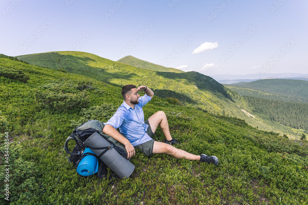 mountain hiking concept. a guy with a big backpack squatting to rest. hiker on top of a mountain