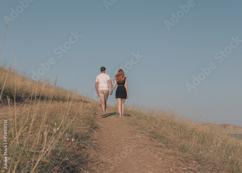 Couple of a man and a girl holding hands, walking across a field, view from the back