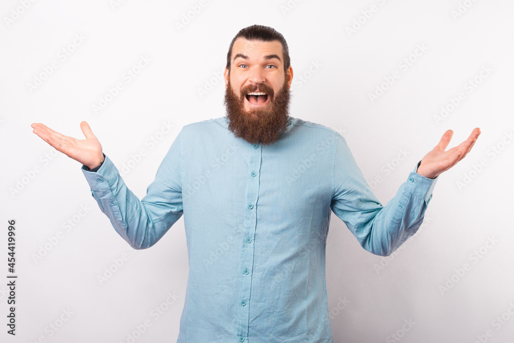 Wide smiling young bearded man shrugs over white background in a studio. Wide smiling young bearded man shrugs over white background in a studio.