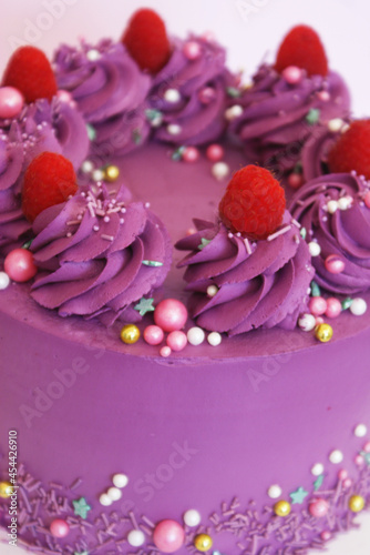 purple cake with raspberry decor, meringues and sweet decorations and on a stand