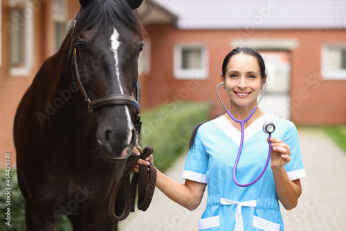 Smiling female veterinarian doctor holding stethoscope next to horse