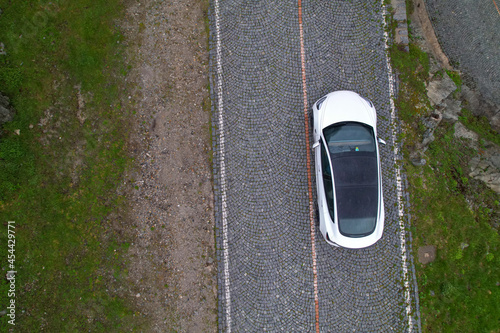 TOP DOWN: Modern white car cruises along empty cobblestone road in Switzerland.