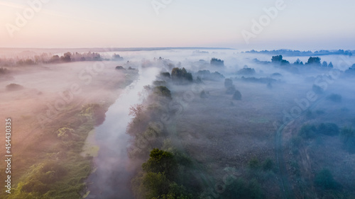 Aerial panoramic view of misty countryside in the summer morning hour with river, meadows, trees.