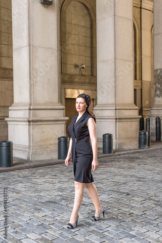 Obraz na płótnie Dressing in black sleeveless clothes a pretty woman is walking outside an office building.. w salonie