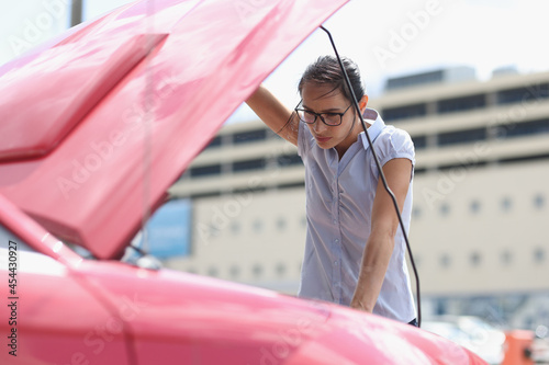 Woman driver opened hood of car and looks at breakdown closeup