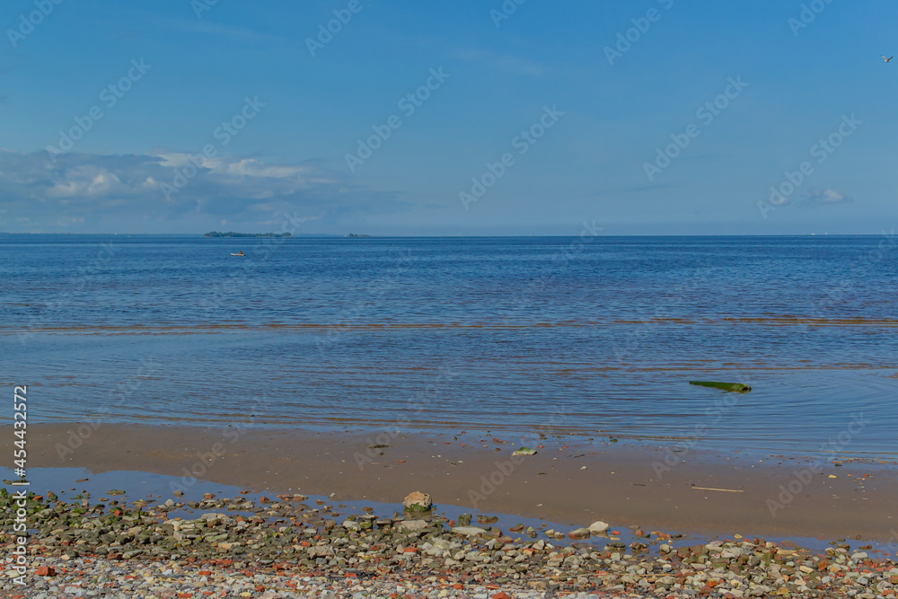 Sandy pebble shore of the northern baltic sea with green and red stones, blue sky with clouds