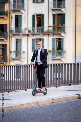 Handsome businessman in suit riding an electric scooter while commuting to work in the city. Ecological transport concept © damianobuffo