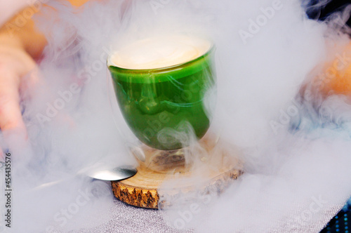 Green cup of coffee on a wooden stand in the smoke