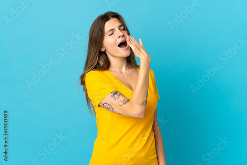 Young slovak woman isolated on blue background yawning and covering wide open mouth with hand