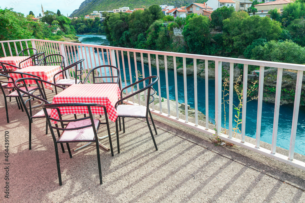 Terrace with chairs and tables at Neretva riverside in Mostar , Bosnia and Herzegovina . 