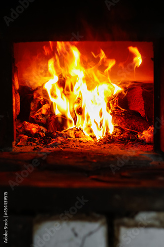 Defocus fire flame background. Firewood burning in old stove or oven. Dark and black. Orange flame. Heat energy. Open iron door. Rustic house. Vertical. Out of focus
