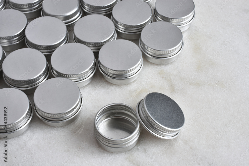 A close up image of several small silver metal sample tins on a white marble table top. A close up image of several small silver metal sample tins on a white marble table top.