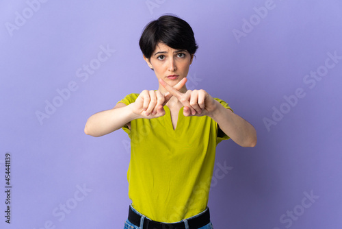 Woman with short hair isolated on purple background making stop gesture with her hand to stop an act © luismolinero